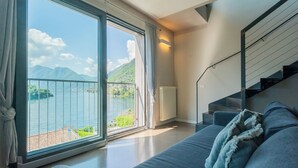A modern living room with a large sliding glass door leading to a balcony with a view of mountains and water. - Mulino Vista Lake by Rent all Como (Tremezzina)