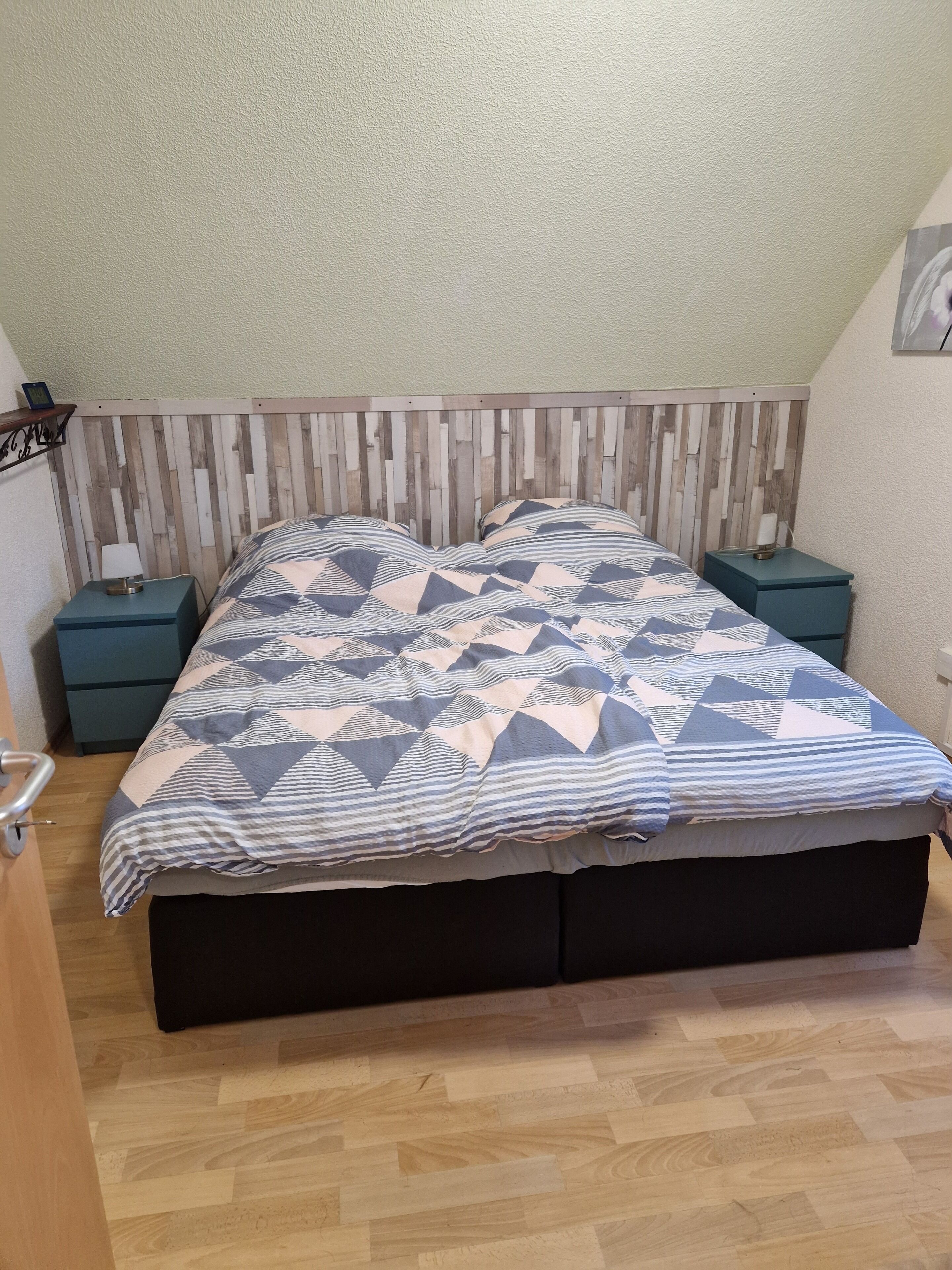 A bedroom with a bed, two nightstands, a wooden headboard, a wall-mounted shelf, and a door.