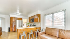 A modern kitchen with wooden cabinets, a stainless steel refrigerator, and a central island with bar stools. - 13 Mi to Downtown Detroit: Bright Home (Dearborn)