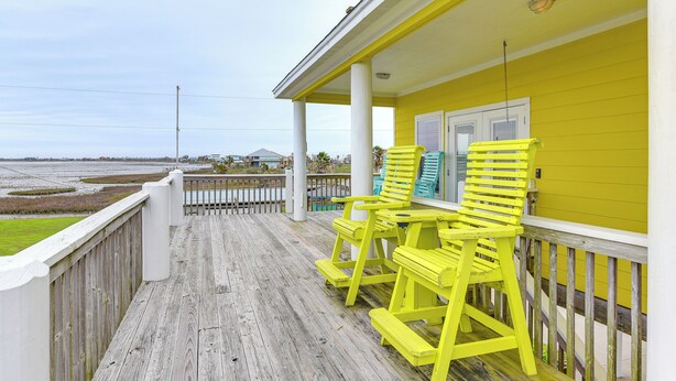 A wooden deck with a yellow railing and two yellow Adirondack chairs.
