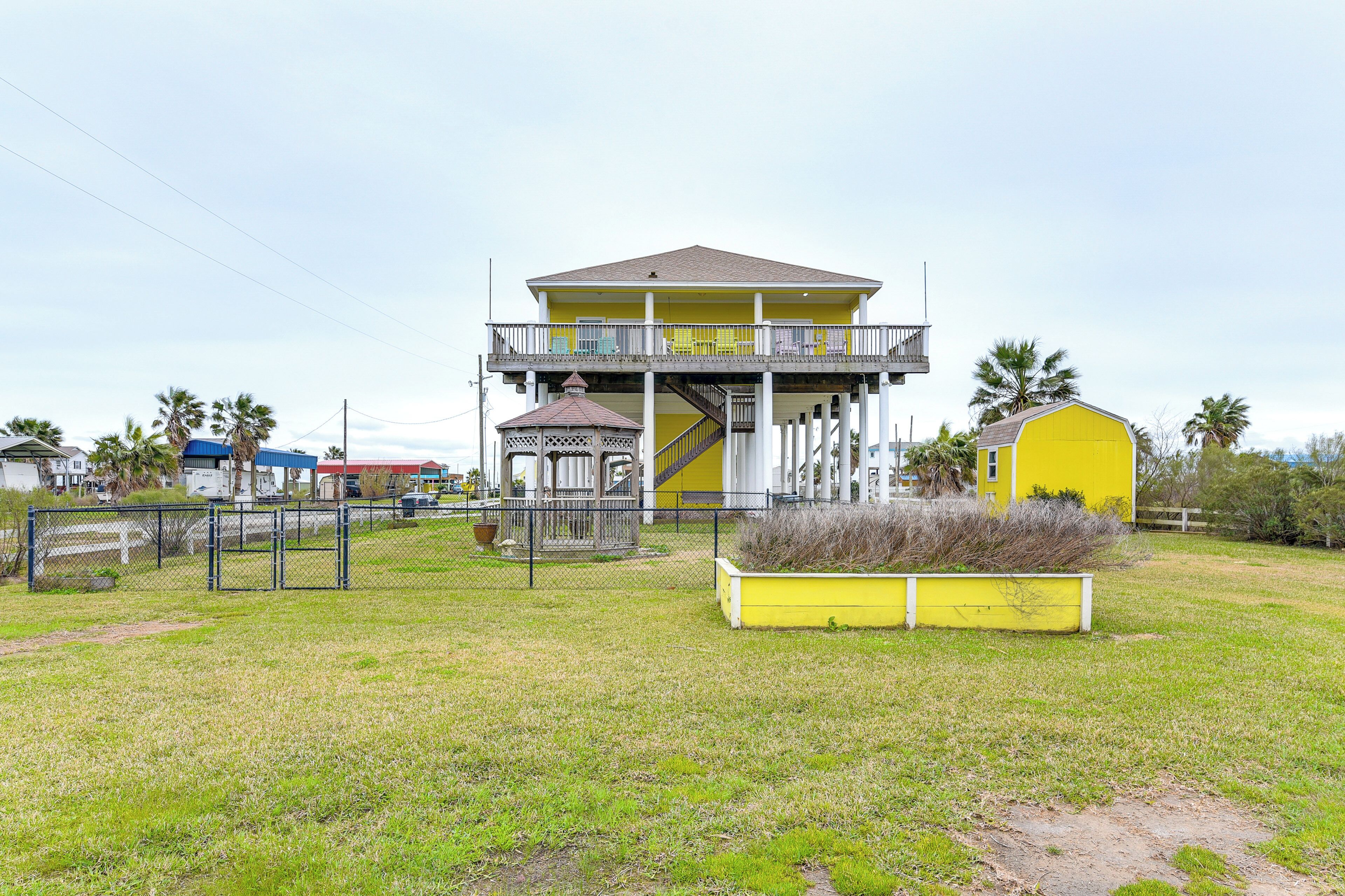 A yellow building with a balcony, a small gazebo, and a fenced area with a planter.
