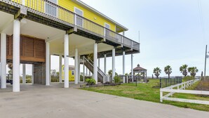 A yellow building with a covered outdoor area supported by columns, a staircase, and a fenced garden area.