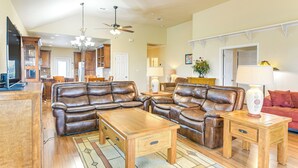 A spacious living room with leather sofas, wooden coffee tables, and a ceiling fan.
