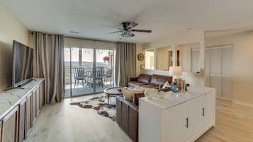 A modern living room with a television, sofa, coffee table, and a dining area with chairs and a table.