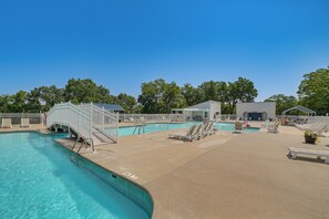 Une piscine entourée d’une clôture blanche, avec des chaises longues et un espace abrité.