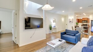 A modern living room with a flat-screen TV, a blue sofa, a coffee table, and a dining area with a kitchen in the background. - 3 Mi to Old Town: Albuquerque Townhome w/ Yard! (Albuquerque)