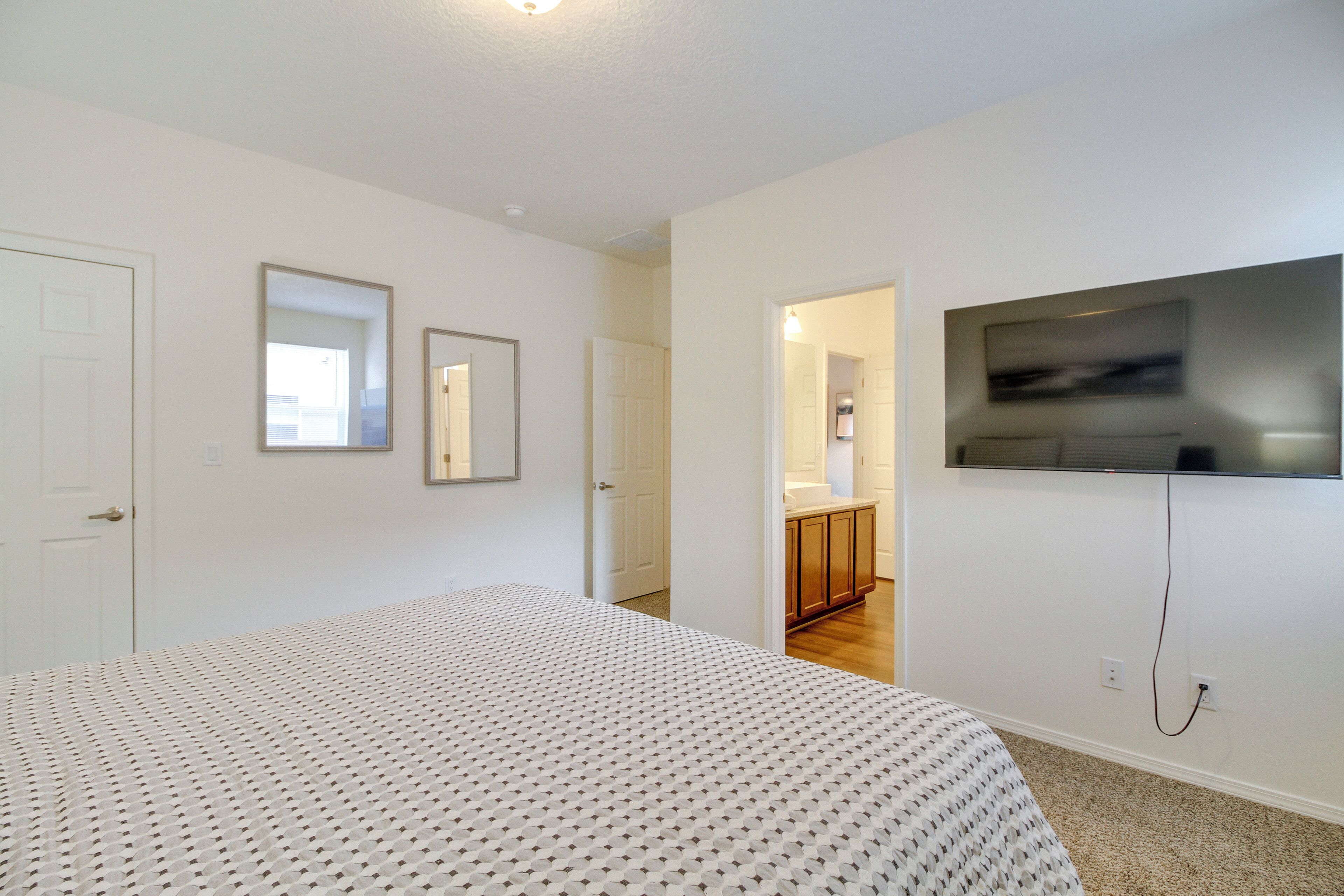 A bedroom with a bed, a TV mounted on the wall, and a door leading to a bathroom.
