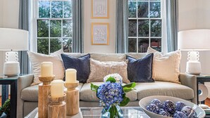 A living room with a sofa, cushions, a coffee table with candles, a vase with flowers, and a bowl of decorative items.