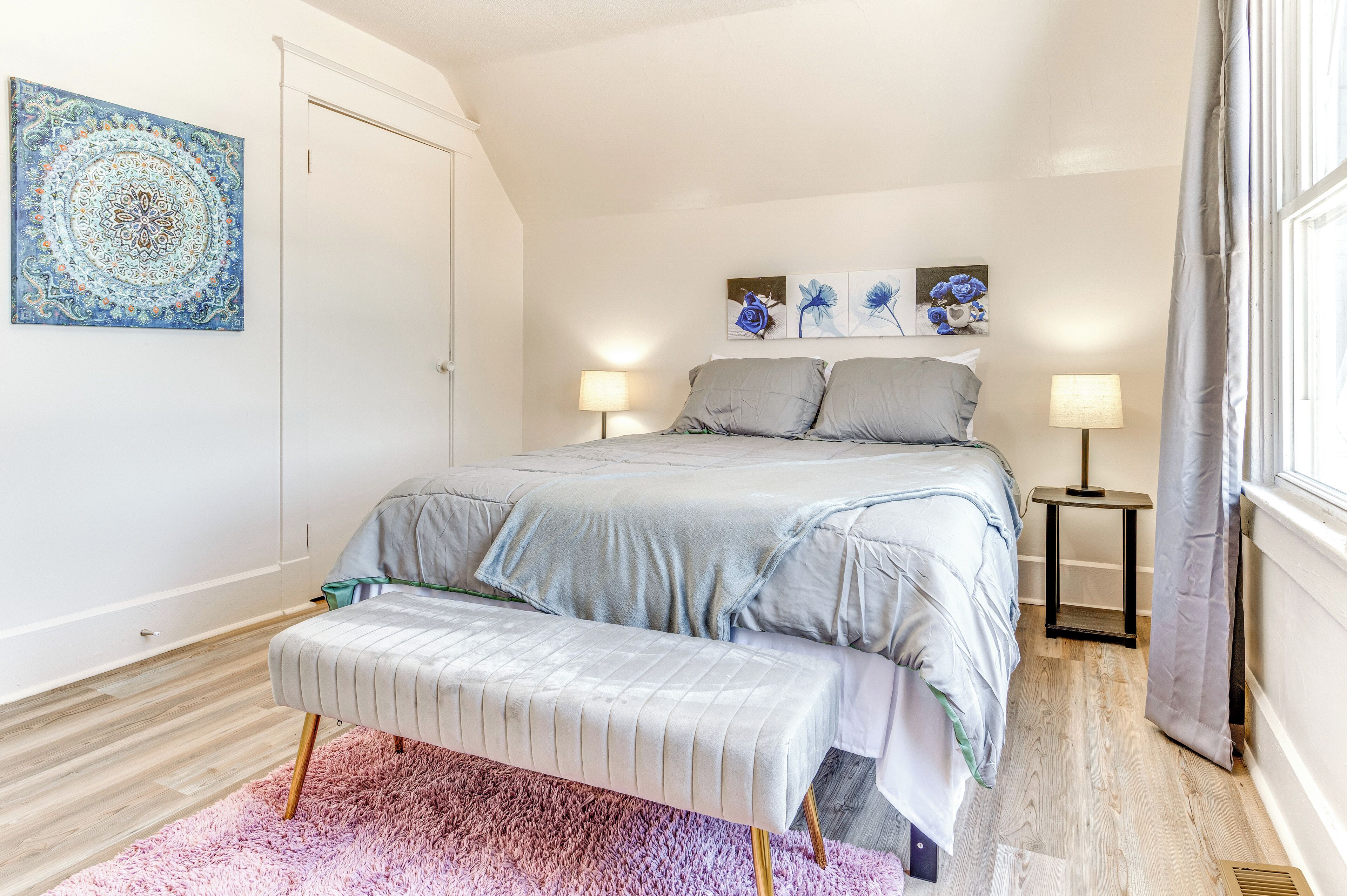 A bedroom with a bed, bench, two bedside tables, and wall art.