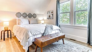 A bedroom with a large bed, bedside lamps, a bench, and a window with curtains. - 3 Mi to Dtwn Indy: Pet-friendly Home w/ Backyard! (Indianapolis)