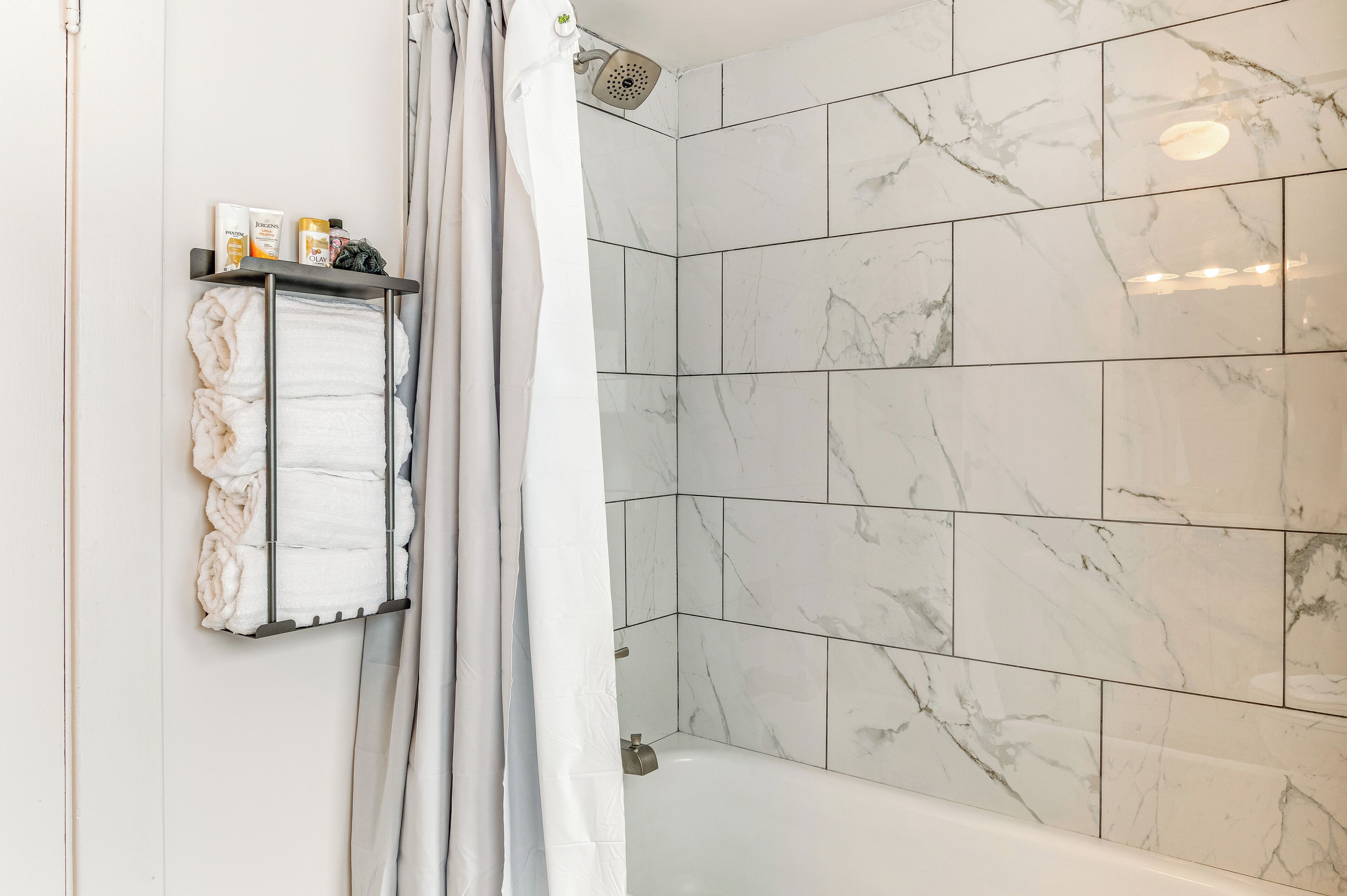 Een badkamer met een douche, een bad en een handdoekrek met opgevouwen handdoeken.