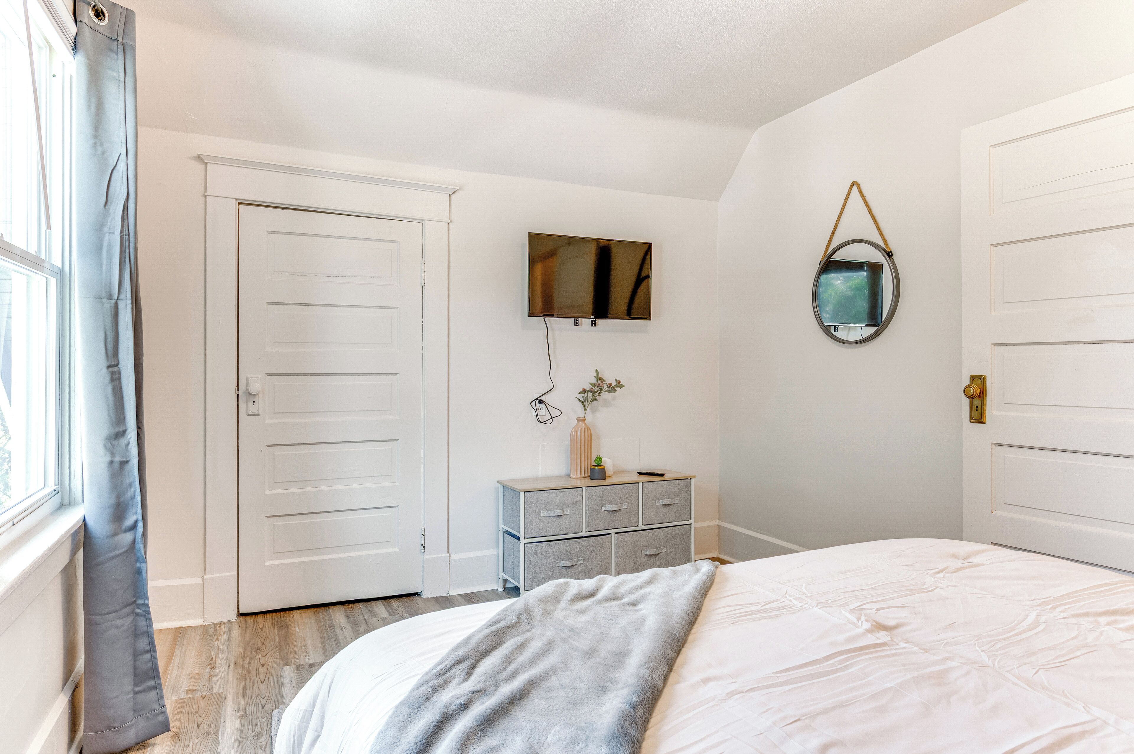 Une chambre à coucher avec un lit, une commode, un téléviseur fixé au mur et une porte.