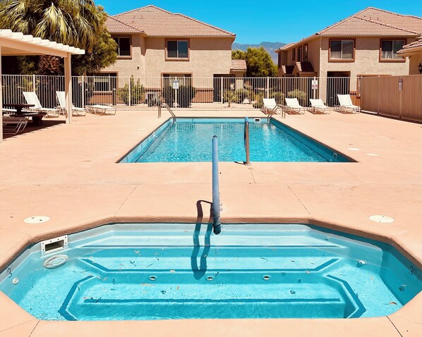 A swimming pool area with two pools, lounge chairs, and a covered seating area.