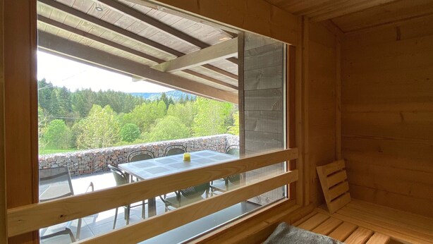 A wooden cabin with a large window overlooking a stone wall and a table with chairs. - Renovated chalet with sauna, near Gérardmer (Sapois)