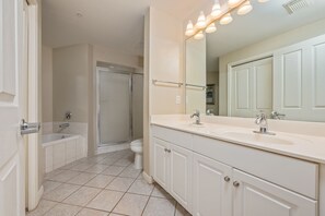 Een badkamer met een bad, toilet en douche. Er is een grote spiegel, een wastafelmeubel met een wastafel en een handdoekhouder.