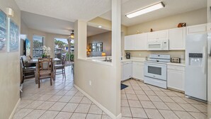 Una cocina moderna con armarios blancos, horno empotrado y microondas. Hay una zona de comedor con sillas de madera y una mesa.