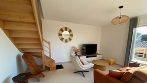 Ein modernes Wohnzimmer mit einer Holztreppe, einer runden Wanduhr, einem Flachbildfernseher, einem weißen Sofa, einem orangenen Sofa und einem kleinen Holztisch.