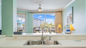 A modern kitchen with a large window, a ceiling fan, and a view of a building and palm trees.