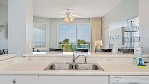 A modern kitchen with a double sink, a ceiling fan, and a view of the outdoor patio. - G316 Gulf-view 2BR+ bunk room w/ balcony, pool access & free beach service (Fort Walton Beach)