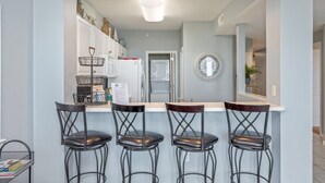 A kitchen with a white countertop, three black bar stools, a white refrigerator, and a white oven. - G316 Gulf-view 2BR+ bunk room w/ balcony, pool access & free beach service (Fort Walton Beach)