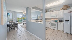 A modern kitchen with white cabinets, a central island, and a view to the outside. - G316 Gulf-view 2BR+ bunk room w/ balcony, pool access & free beach service (Fort Walton Beach)
