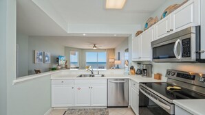 A modern kitchen with white cabinets, stainless steel appliances, and a large window offering a view. - G501 Corner 2BR + Bunk w/ Gulf Views, Balcony & Free Beach Service (Fort Walton Beach)