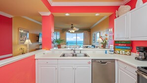 A kitchen with white cabinets, a stainless steel sink, and a dishwasher. There is a large window with a view of the ocean. - G616 Tropical oasis with wraparound balcony, Gulf views & top-tier amenities! (Fort Walton Beach)