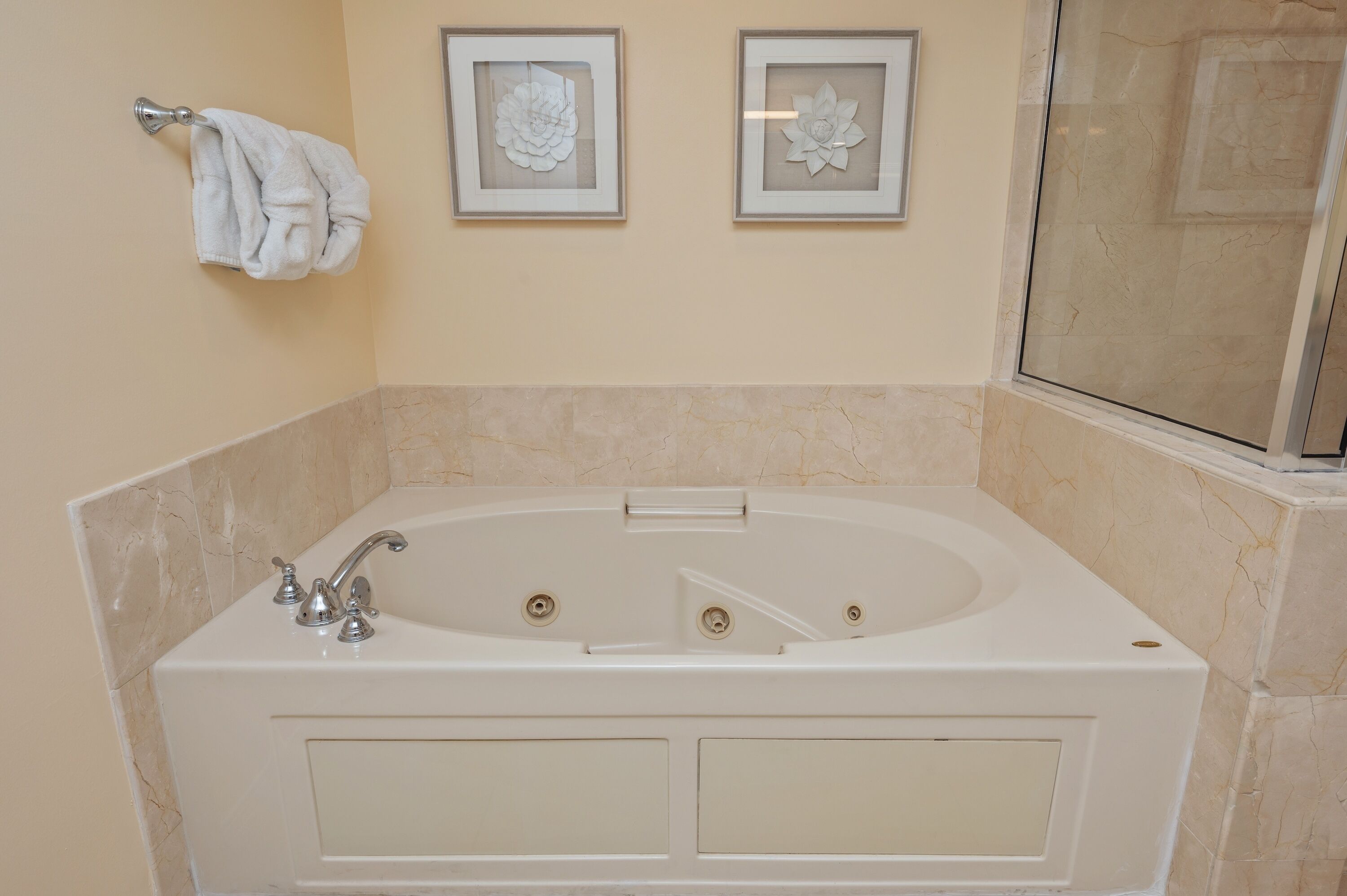 A bathroom with a bathtub, a towel rack, and two framed floral decorations on the wall.