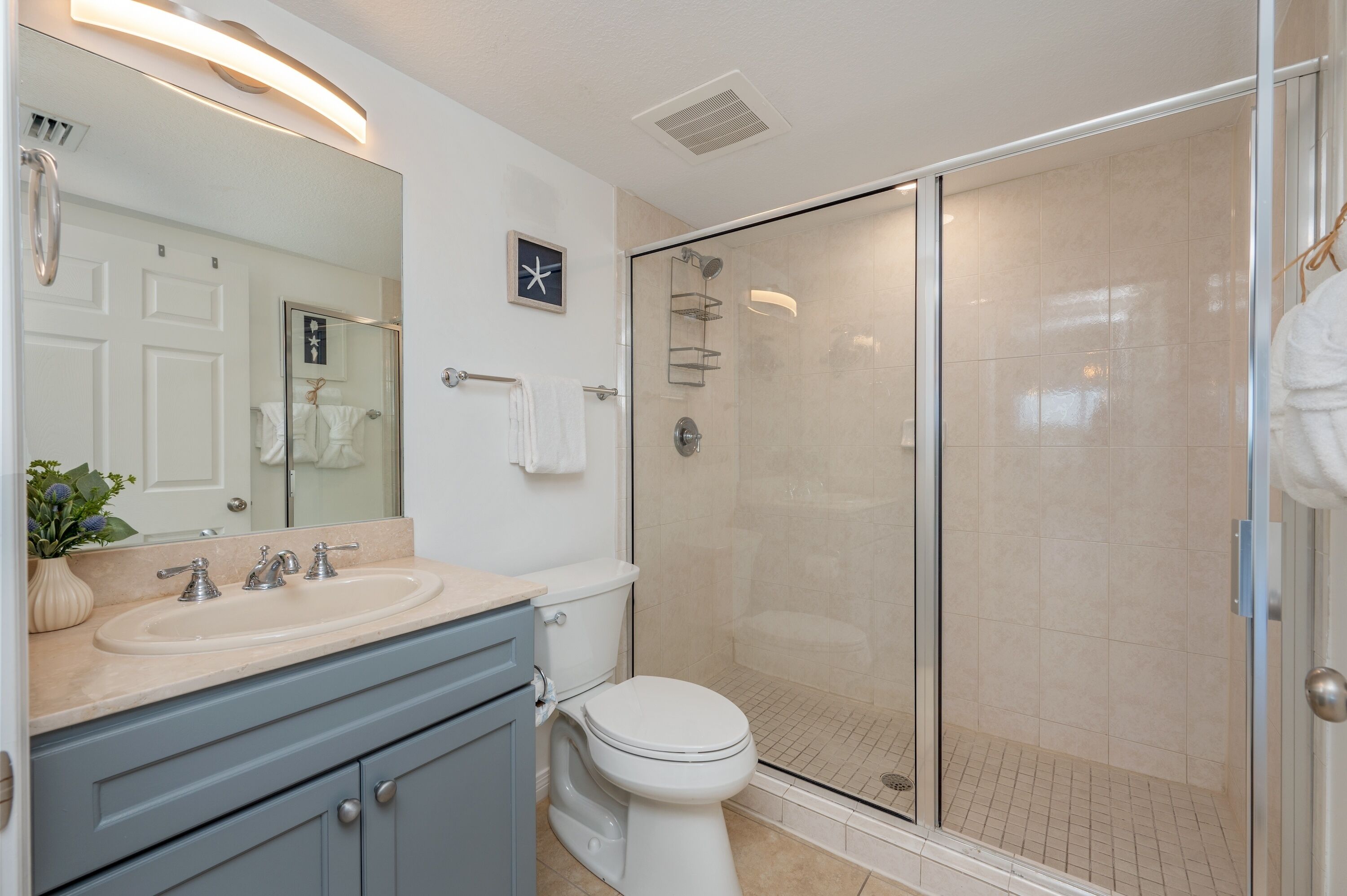 A modern bathroom with a glass-enclosed shower, a large mirror, and a vanity with a sink and cabinet.