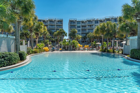 A swimming pool with clear blue water, surrounded by palm trees and a building with balconies.
