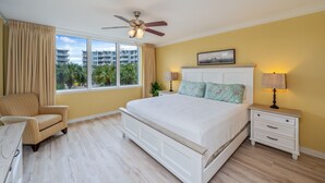 Un dormitorio con cama, mesitas de noche, una silla y un ventilador de techo.