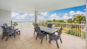 Un balcón con mesa y sillas, con vista a una playa y palmeras.