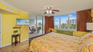 A hotel room with a large bed, a ceiling fan, a TV on the wall, a small table with a plant, and a view of the outside balcony. - Heron 406 | Bay & Lazy River Views | Spacious 3BR Retreat w/ Balcony! (Ft. Walton Beach)
