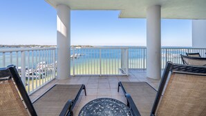A balcony with a view of the sea, white railings, and two wicker chairs. - H602 Top-Floor 3BR Bayfront Condo | Stunning Views | Free Beach Service! (Ft. Walton Beach)