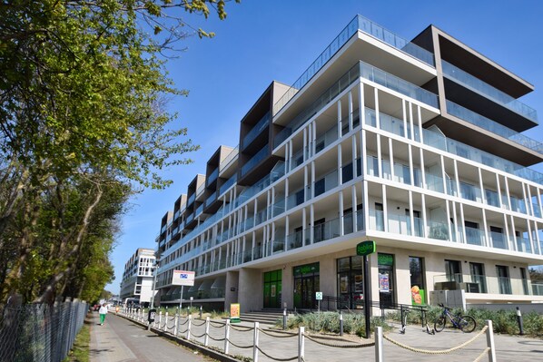 A modern multi-story building with a glass facade, outdoor seating area, and a bike parked outside. - RentPlanet - Perłowa Przystań (Sianożęty)