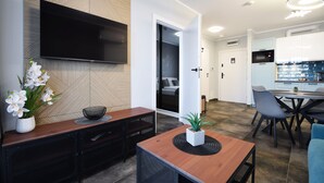 A modern living room with a flat-screen TV, a wooden coffee table, and a dining area with a table and chairs. - RentPlanet - Perłowa Przystań (Sianożęty)