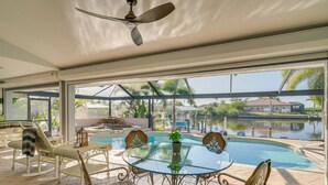 A glass-enclosed patio with a pool, outdoor furniture, and a view of a lake and buildings.