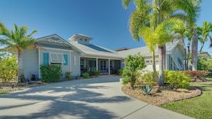 A two-story house with a covered porch, a driveway, and surrounding palm trees.