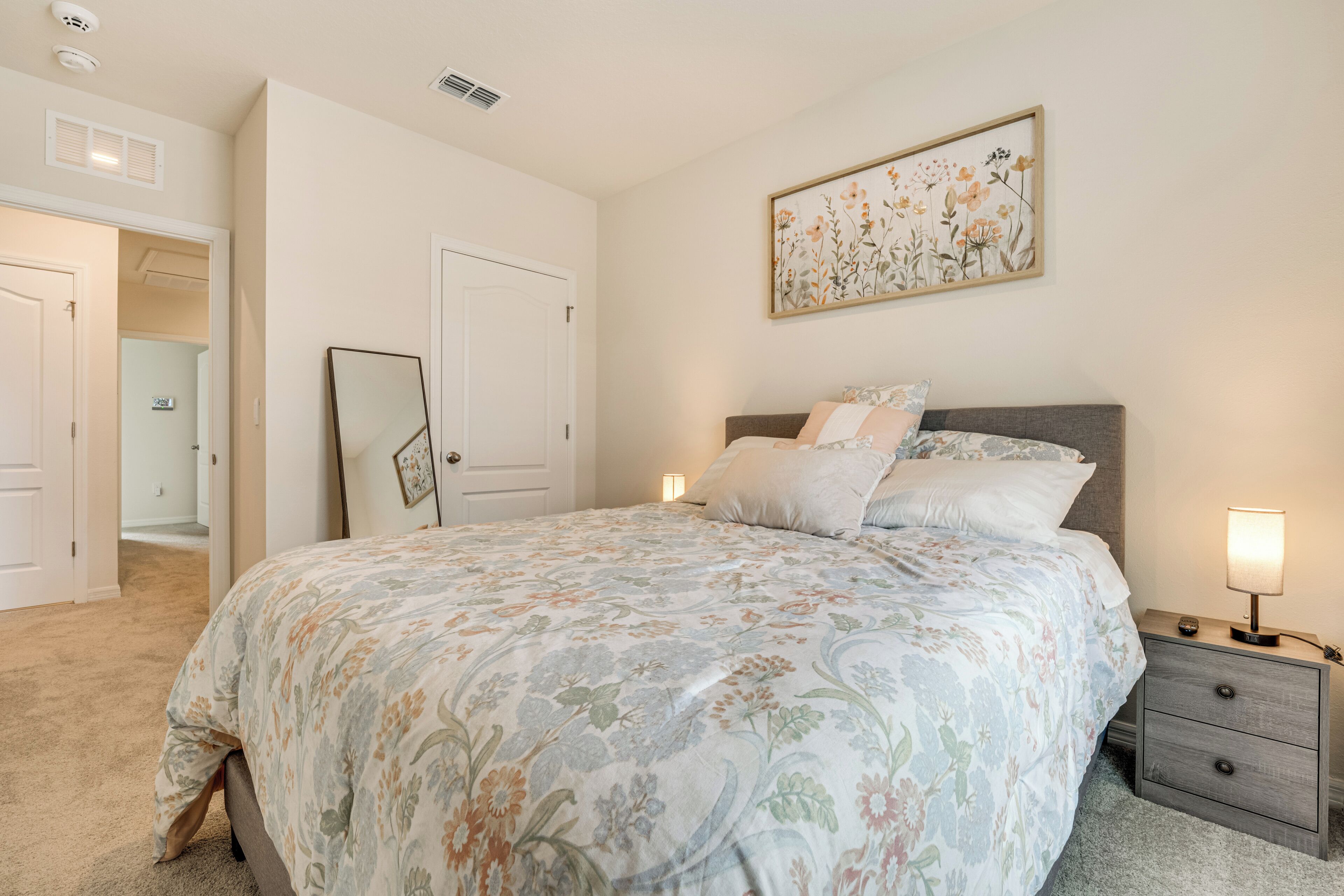 A bedroom with a floral bedspread, a bedside table with a lamp, and a framed picture on the wall.