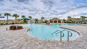 A swimming pool with a curved design, surrounded by lounge chairs and palm trees. - Davenport Home w/ Pool Access & Patio! (Davenport)