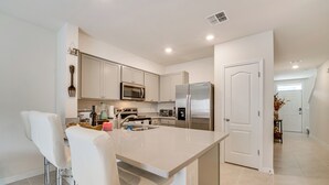 A modern kitchen with white cabinets, stainless steel appliances, and a central island with bar stools. - Davenport Home w/ Pool Access & Patio! (Davenport)