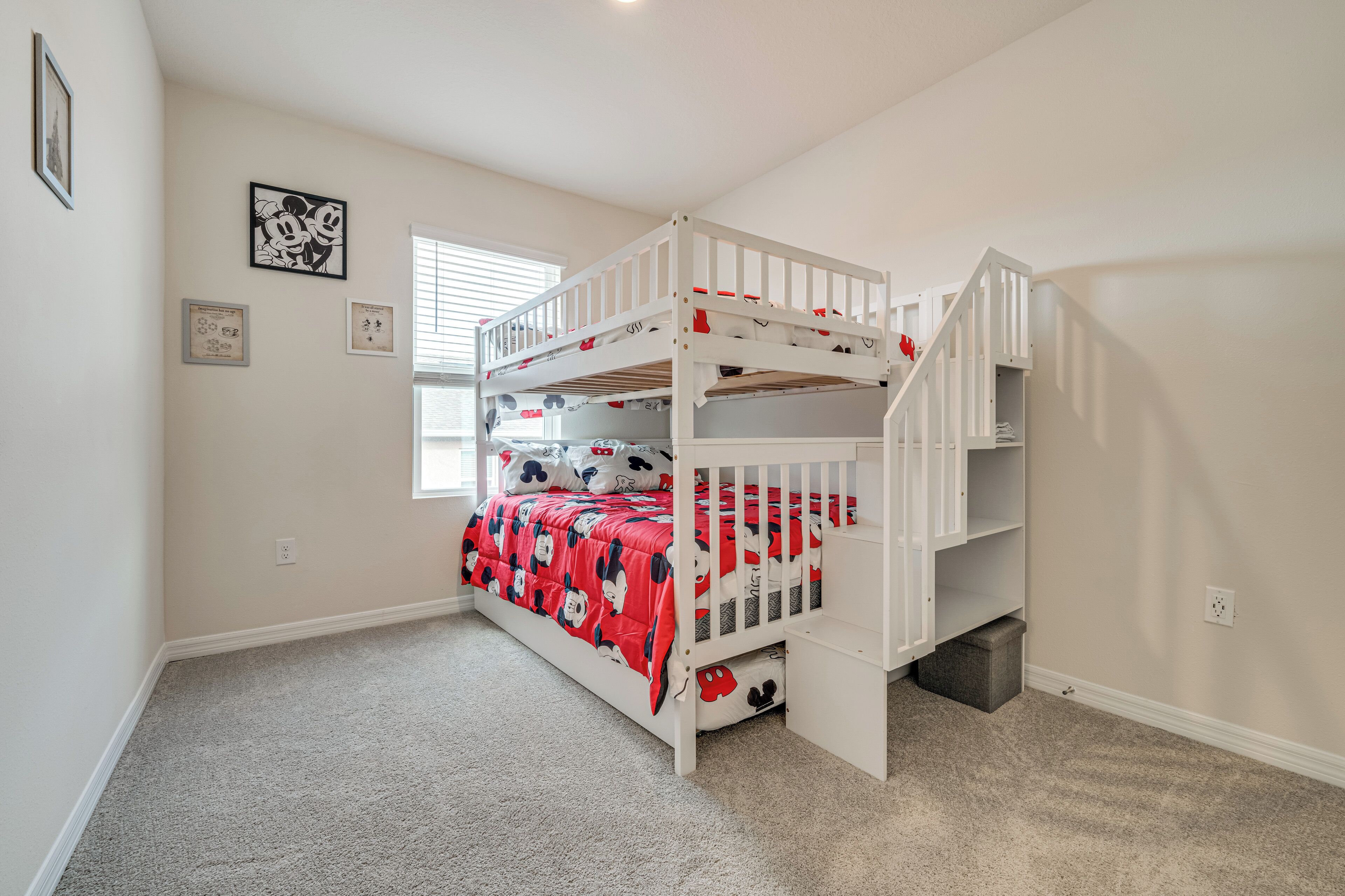 A bunk bed room with a red Mickey Mouse themed bedspread, a small window with blinds, and a framed picture on the wall.