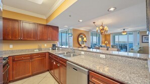 A kitchen with granite countertops, wooden cabinets, a dishwasher, and a large window offering a view. - O503 Spacious Corner Unit | 3BR + Bunk Room | Unobstructed Bay Views & Pools! (Fort Walton Beach)