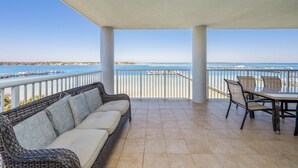 A covered outdoor seating area with a view of the sea, a dining table with chairs, and a wicker sofa. - O503 Spacious Corner Unit | 3BR + Bunk Room | Unobstructed Bay Views & Pools! (Fort Walton Beach)