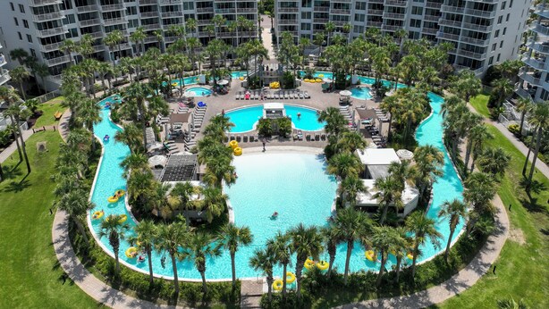 A resort with a central pool surrounded by palm trees and a multi-level building with balconies. - O603 Spacious Bayside Condo | Panoramic Views | Lazy River & Resort Access (Fort Walton Beach)