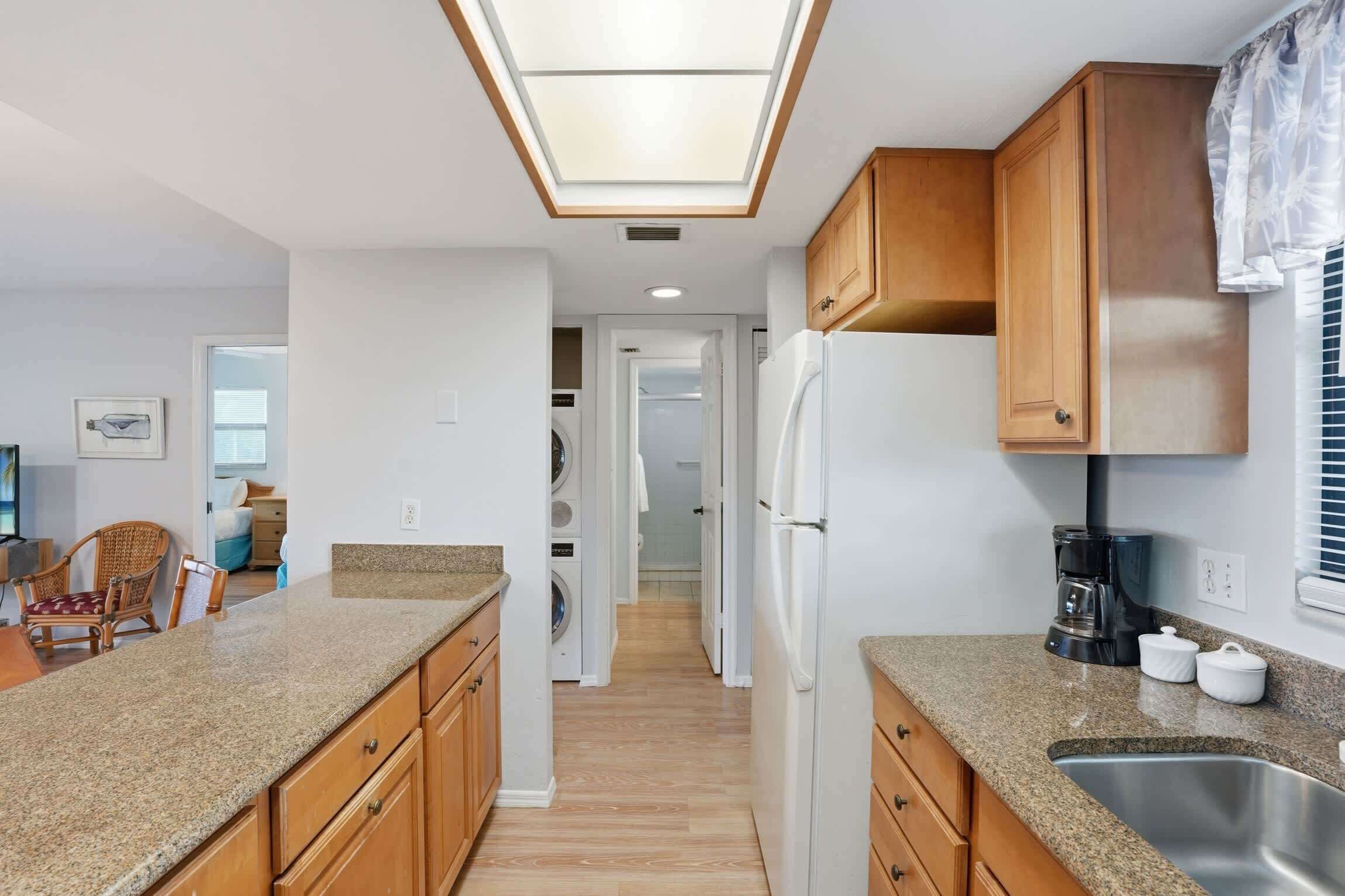 Una cocina compacta con encimeras de granito, armarios de madera, refrigerador integrado y tragaluz.