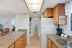 Una cocina compacta con encimeras de granito, armarios de madera, refrigerador integrado y tragaluz.