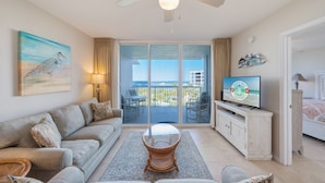 A living room with a sofa, a coffee table, a television, and a balcony with a view of the ocean. - P503 Romantic High-Floor 2BR Condo | Bay & Lazy River Views | Private Balcony (Fort Walton Beach)