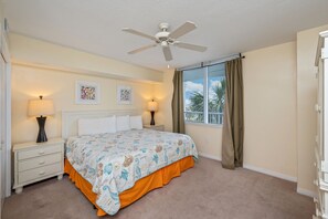 Une chambre à coucher avec un lit, deux lampes de chevet, un ventilateur de plafond et une fenêtre avec des rideaux.