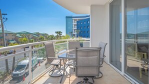 A balcony with a glass table and chairs, overlooking a parking area and a blue building. - V301 Cozy Studio with Gulf Views, Private Balcony and Full Resort Access (Fort Walton Beach)
